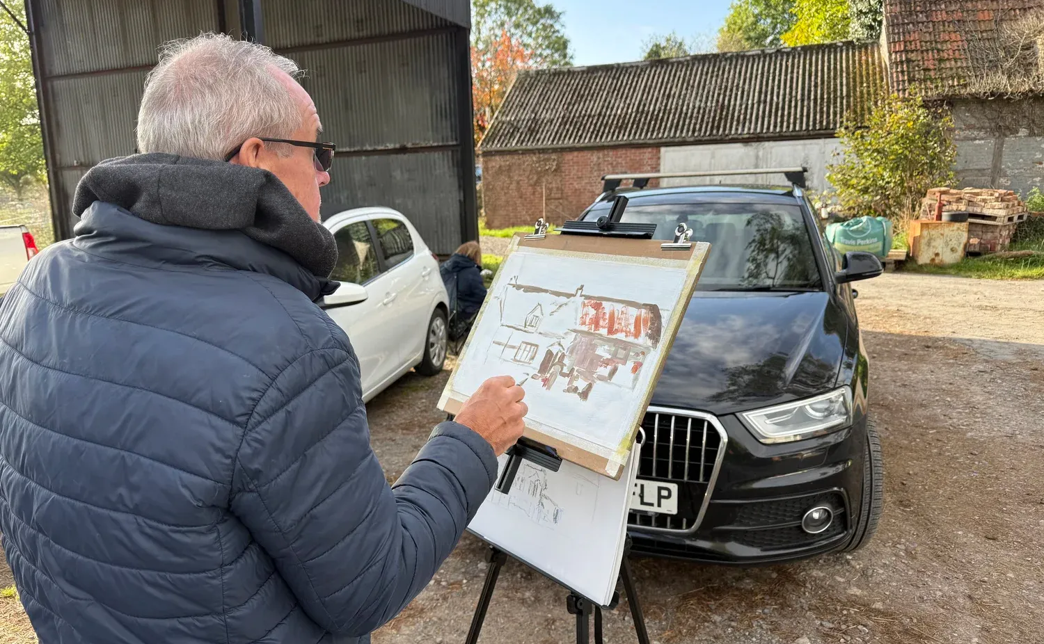 Man painting a black car outdoors in a driveway, with a white car beside him.