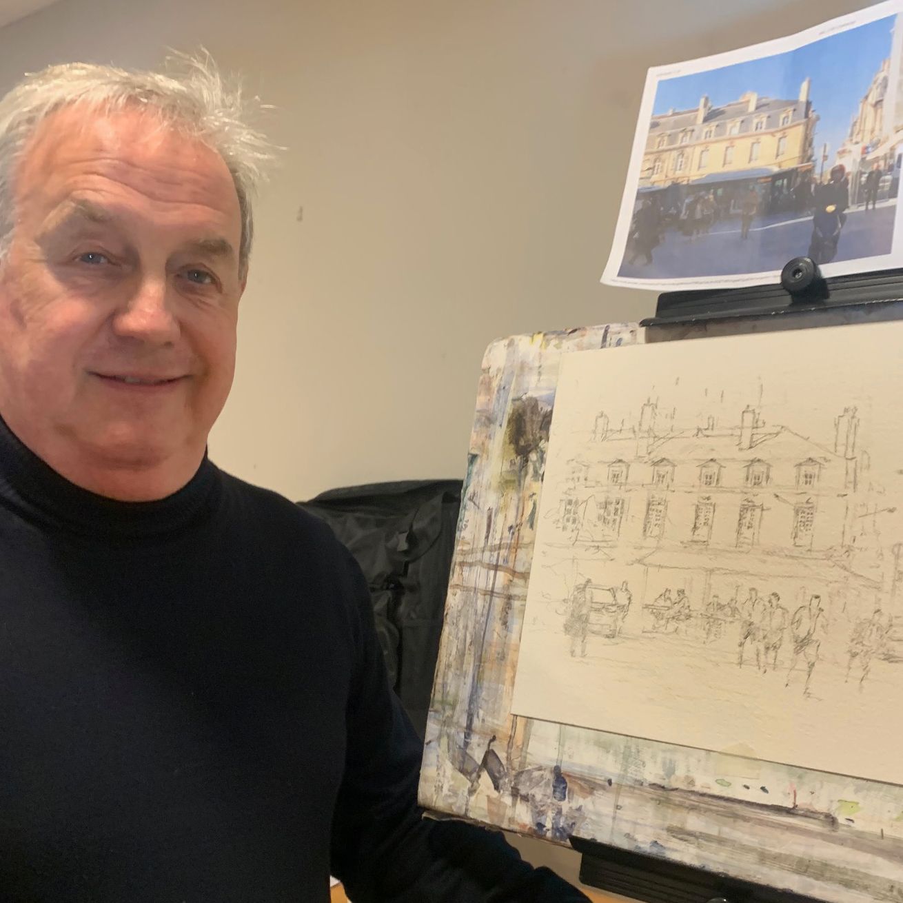 Man standing beside an easel with a sketch of a building and a reference photo above it