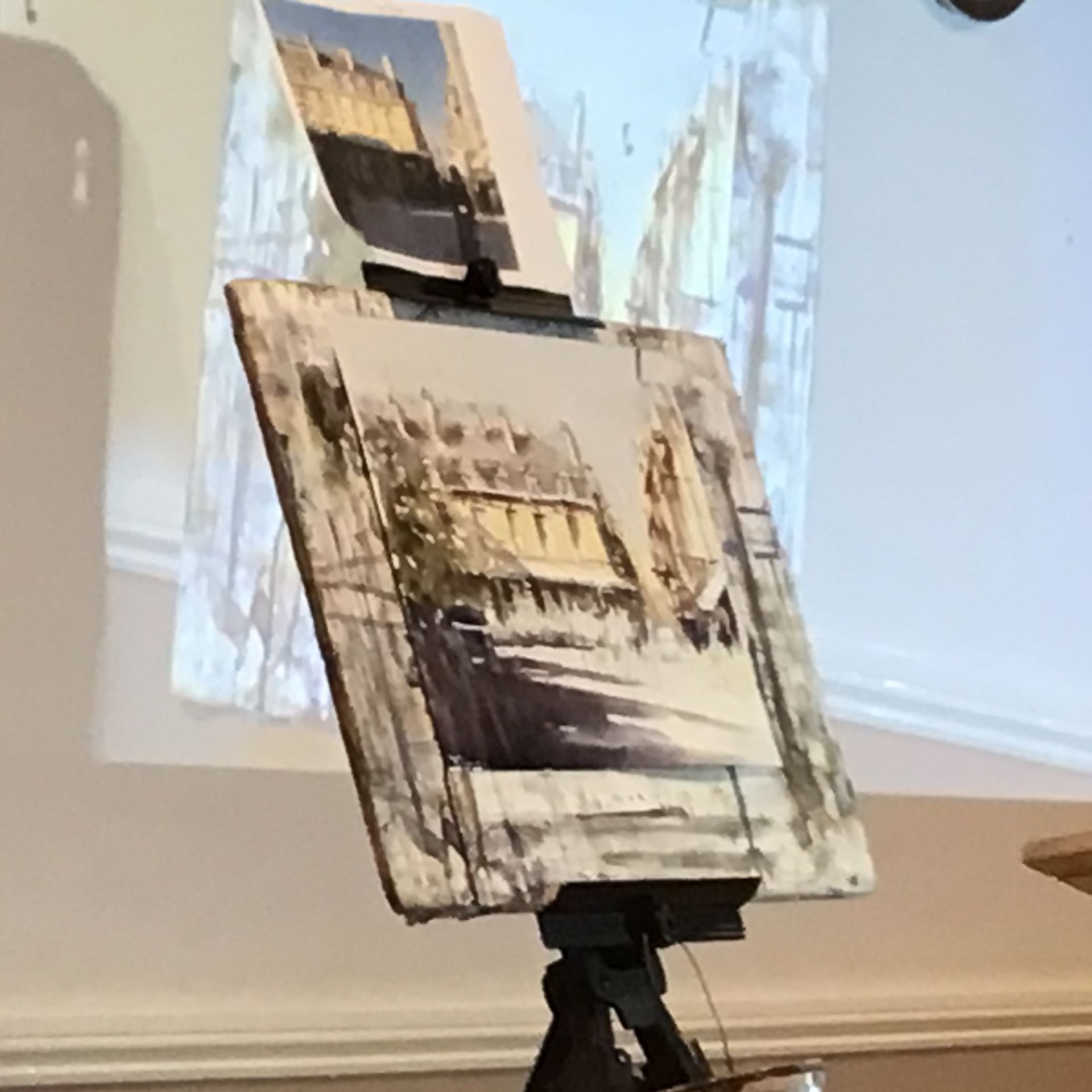 Abstract painting on an easel in a gallery, with layered black, beige, and white brushstrokes.
