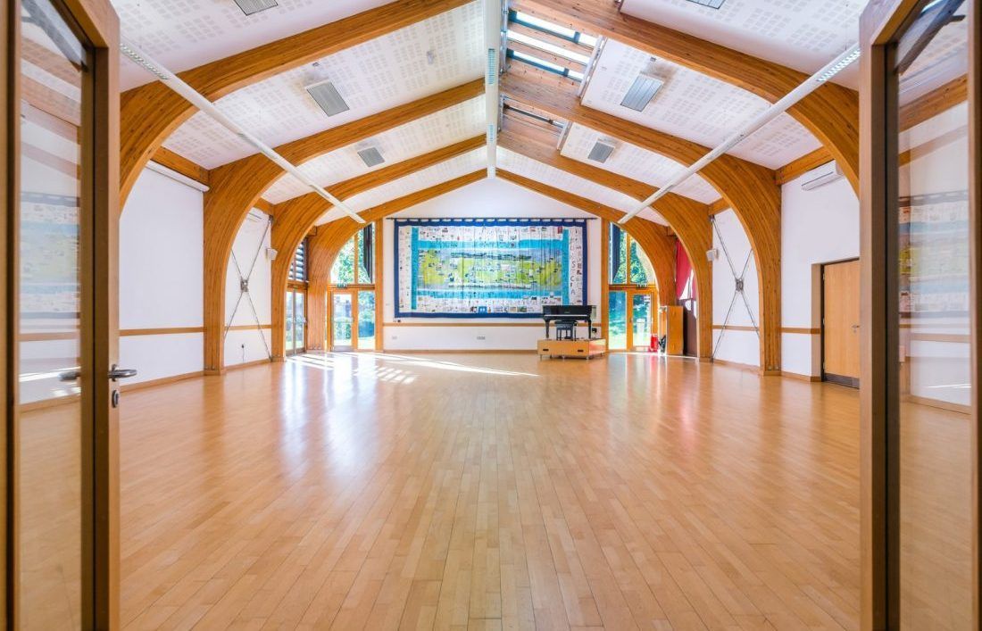 Empty indoor hall with polished wooden floor, arched ceiling, and a colorful stage mural at the far end