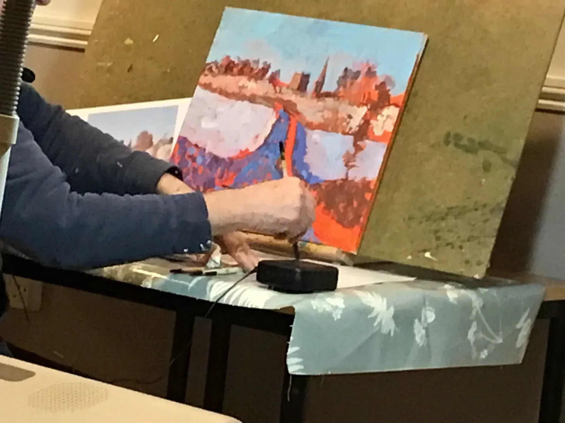 Person painting a colorful landscape on a canvas at a table