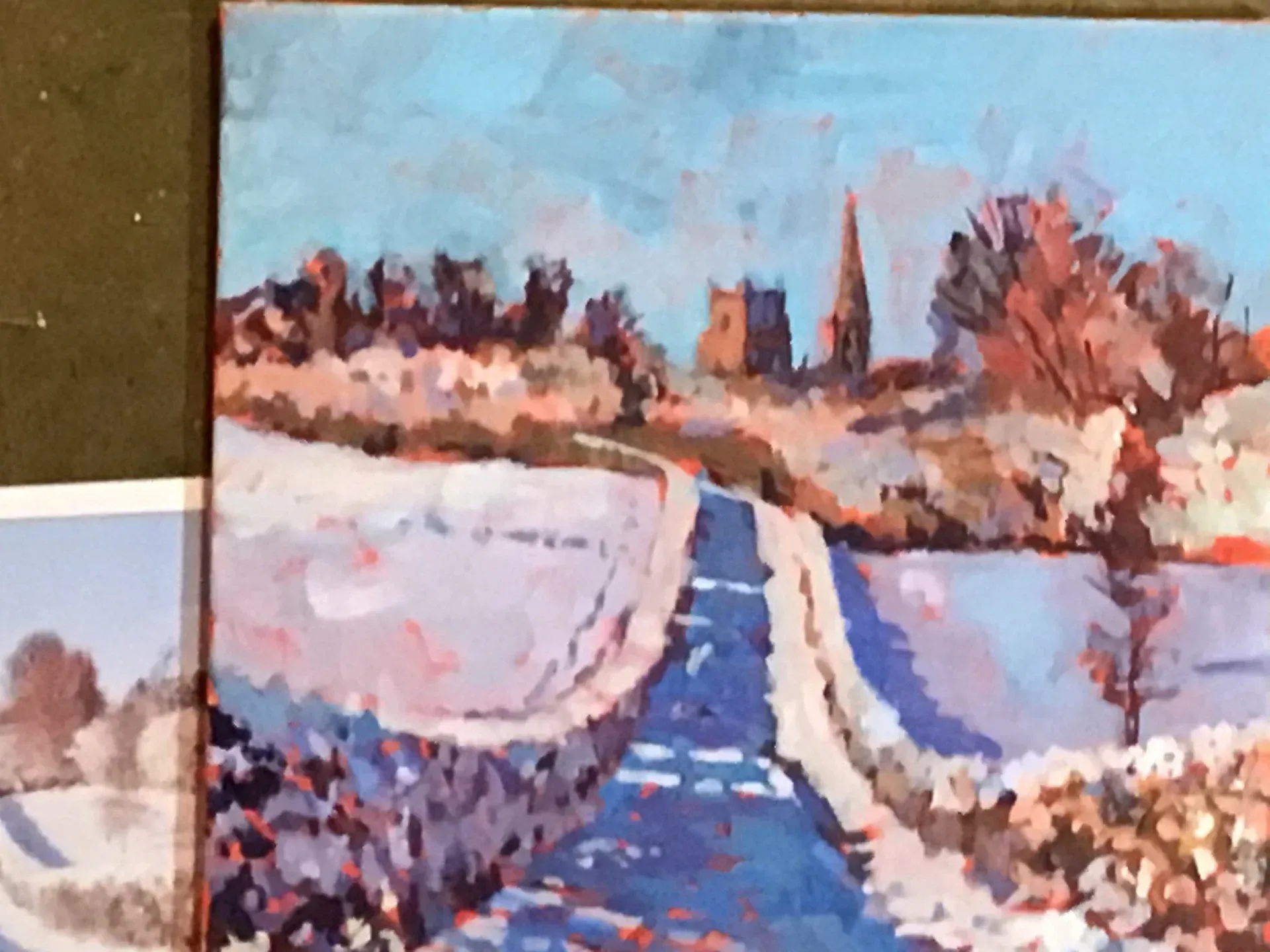 Snowy path leading through fields toward a distant church steeple under a blue sky