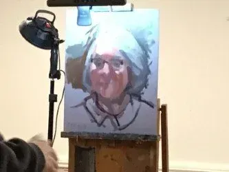 Portrait painting on an easel, lit by a lamp in a plain room.