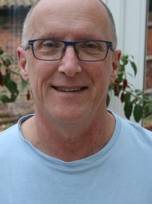 Smiling man wearing glasses and a light blue shirt, standing outdoors.