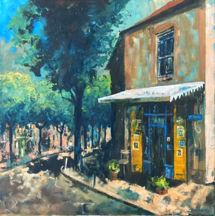 Sunny street with a brick storefront, blue awning, and trees along a quiet sidewalk.
