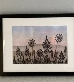 Framed botanical print of silhouetted wildflowers against a pastel sky and hills