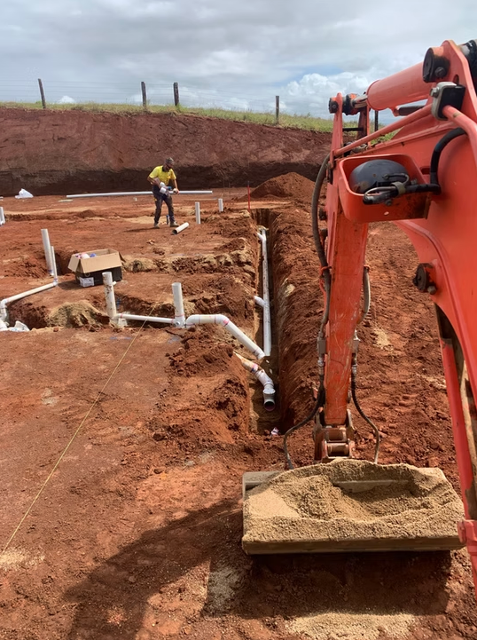 Excavator digging a trench at a construction site with a worker in the background. — Dunnerite Plumbing in Mount Peter, QLD