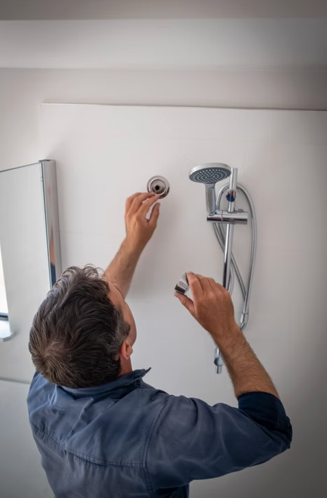 Person installing a showerhead and fixture on a white bathroom wall — Dunnerite Plumbing in Mount Peter, QLD