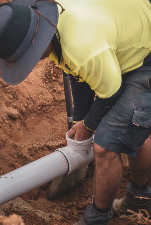 Worker fitting a white PVC pipe joint outdoors, wearing a yellow shirt and dark hat. — Dunnerite Plumbing in Mount Peter, QLD