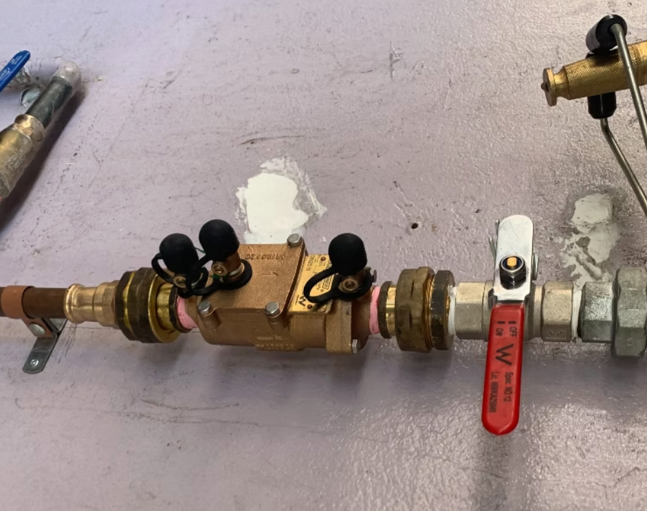 Brass plumbing valve assembly with red and black shutoff handles on a wall-mounted pipe. — Dunnerite Plumbing in Mount Peter, QLD