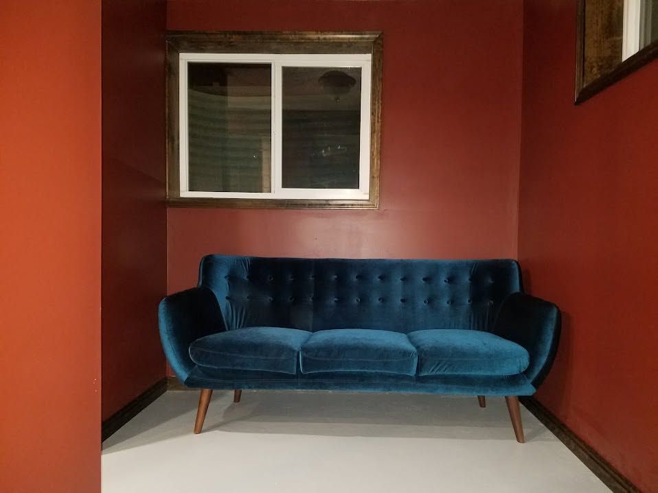 Blue velvet sofa in a red-walled room beneath a window