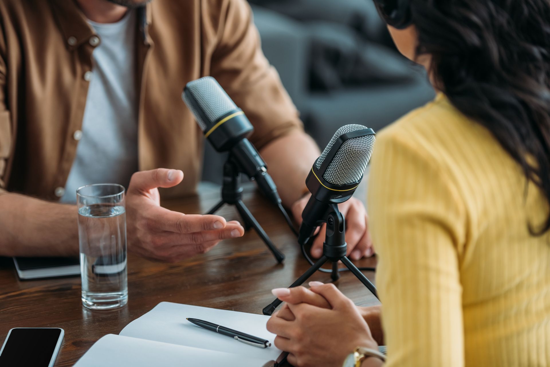 People recording a podcast interview at a table with microphones and a glass of water