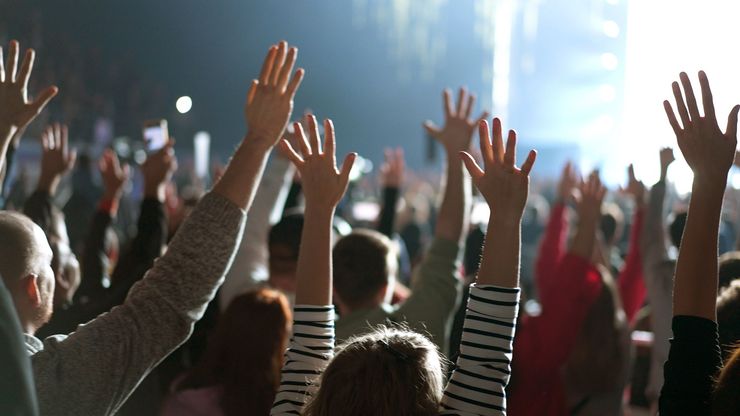 Crowd at a concert with raised hands under bright stage lights
