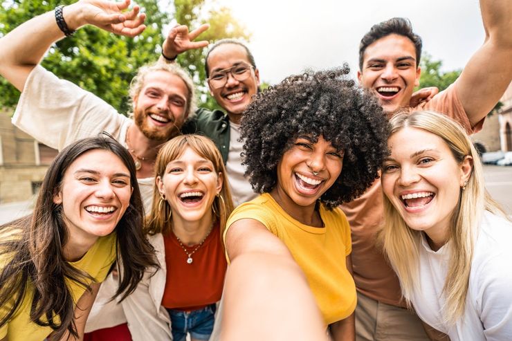 Group of smiling friends taking a selfie outdoors with arms raised