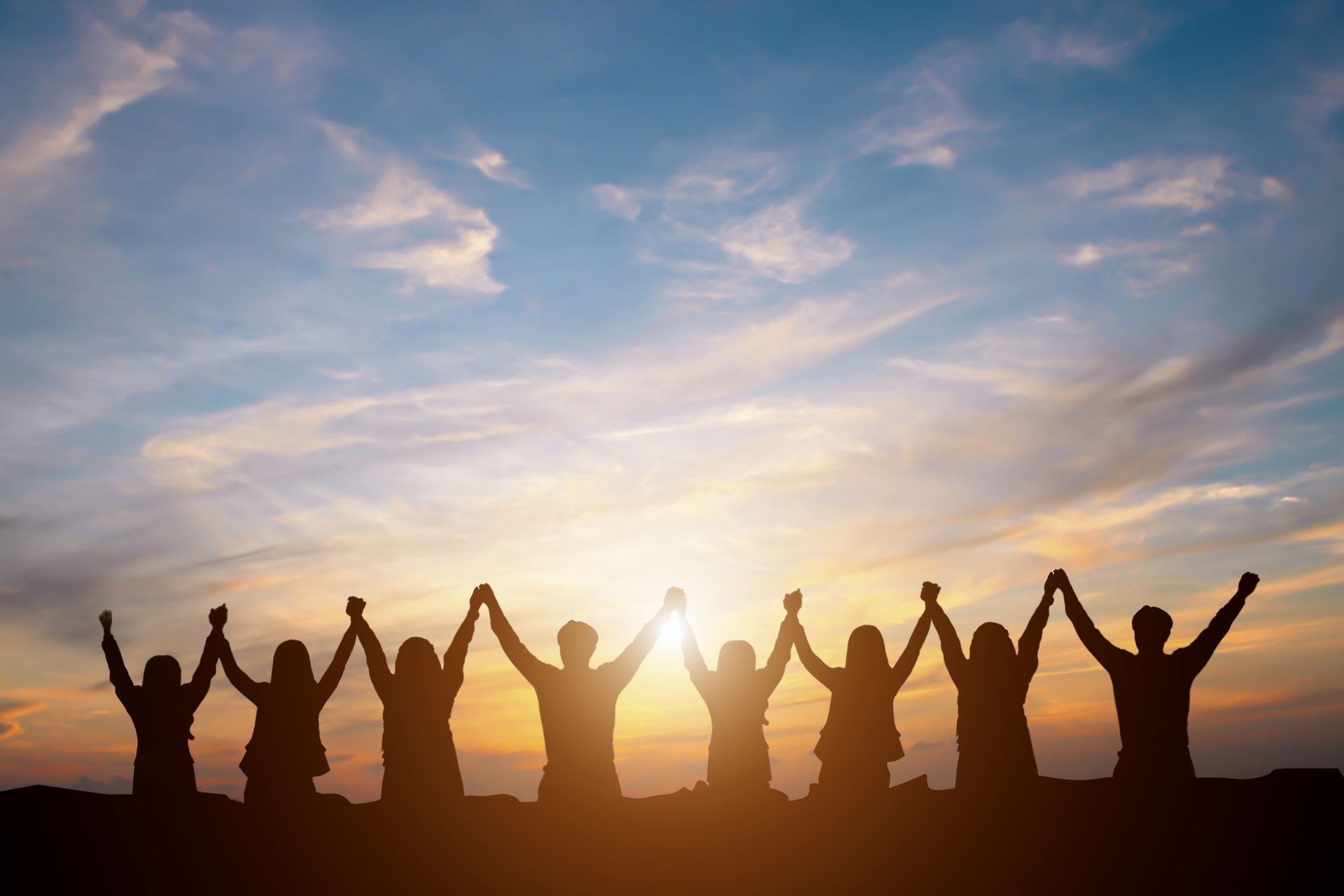 People standing hand in hand at sunset, silhouetted against a colorful sky.