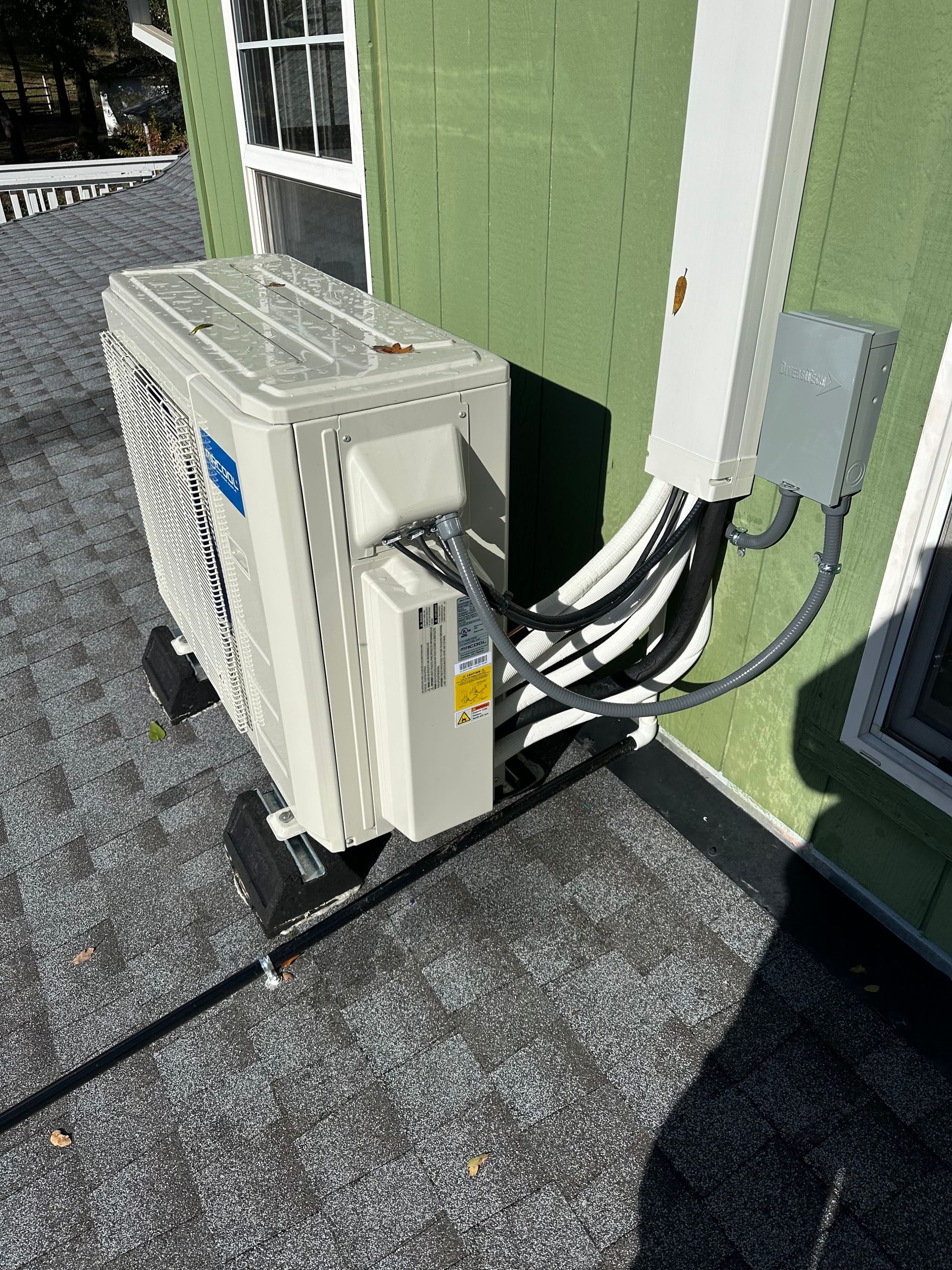 A white air conditioner is sitting on the side of a green house.