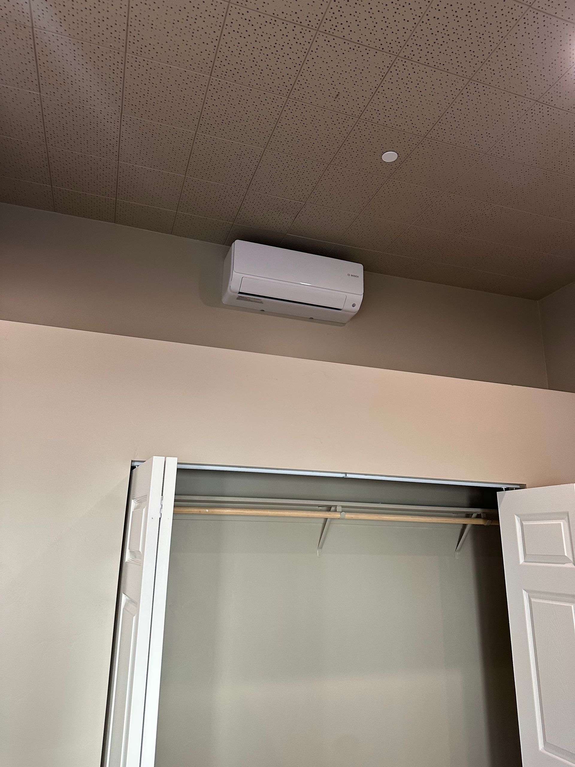 A white air conditioner is mounted to the ceiling above a closet.