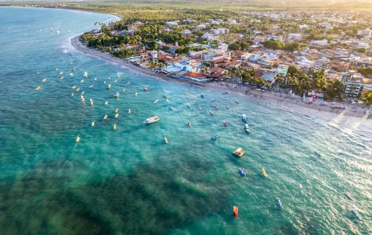 Uma vista aérea de uma praia com barcos na água e uma cidade ao fundo.