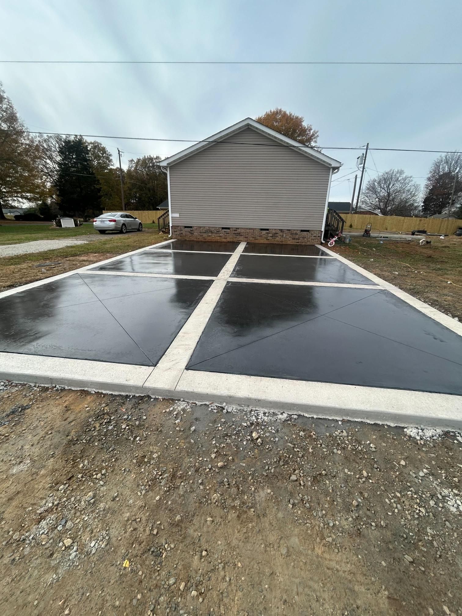 Newly poured concrete driveway with gray blocks, bordered by concrete. A light-colored house is in the background.