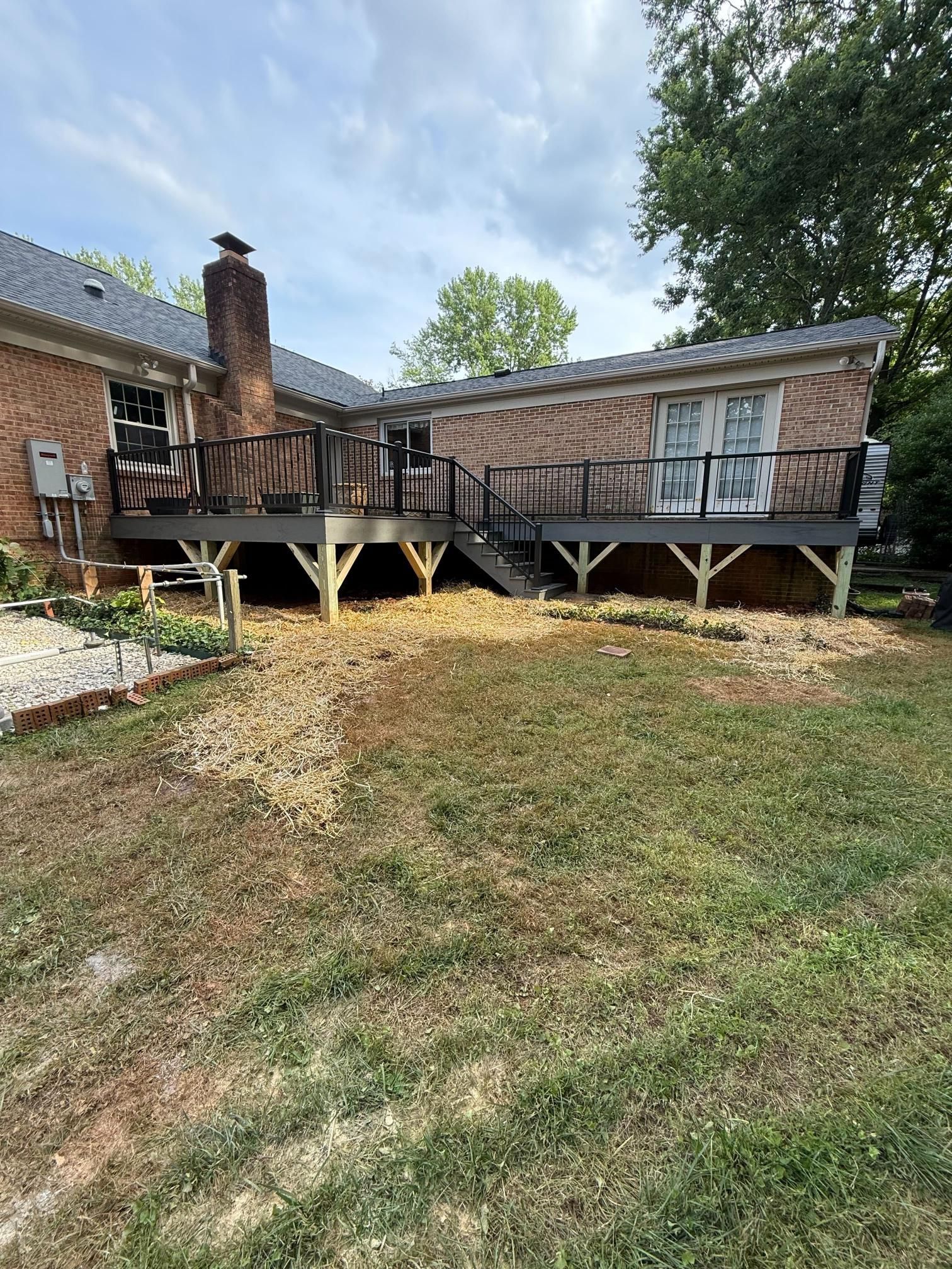 A backyard with a large wooden deck attached to a brick house.