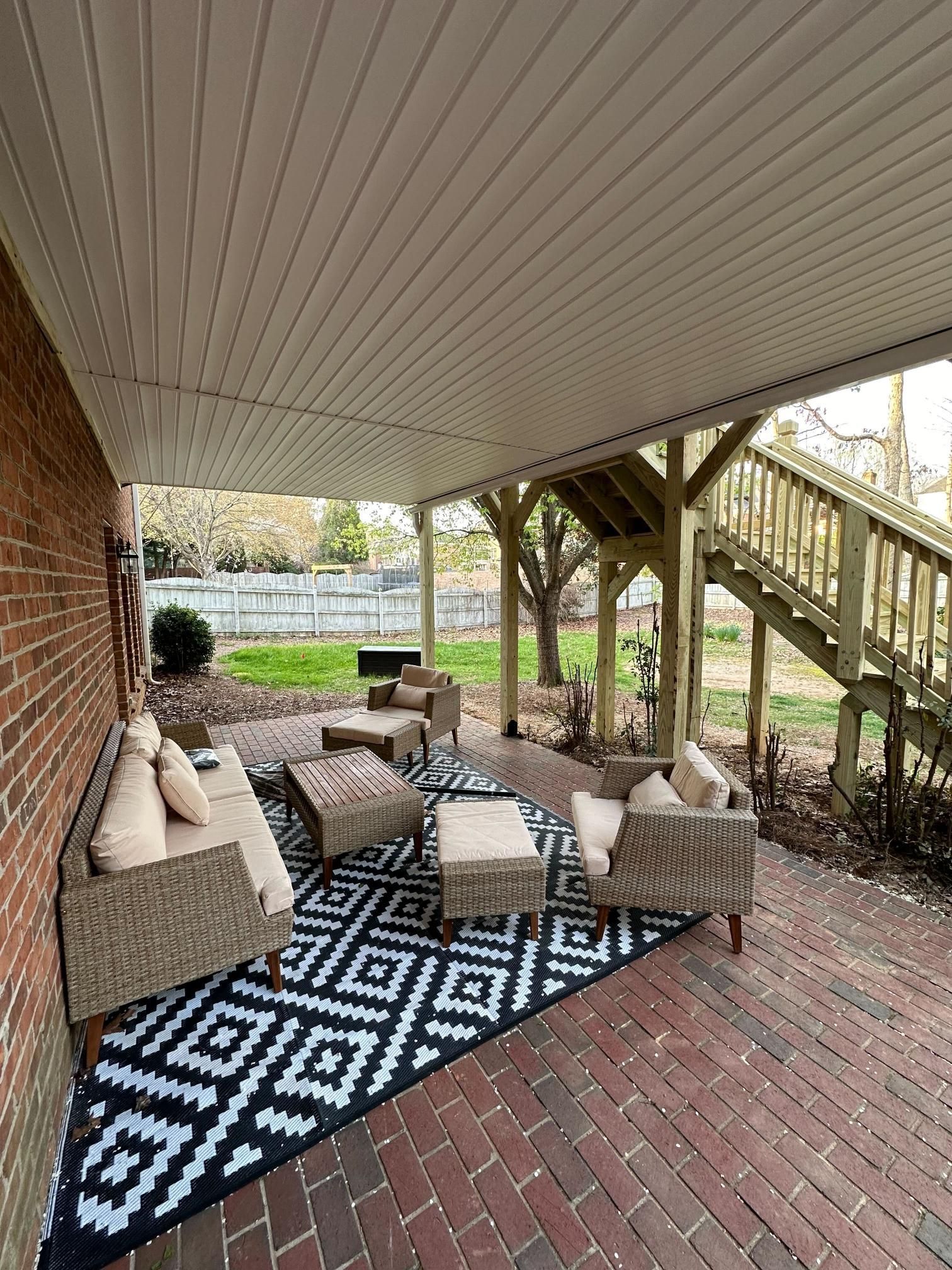 Patio with woven furniture, black and white rug, under a covered area, stairs leading up.