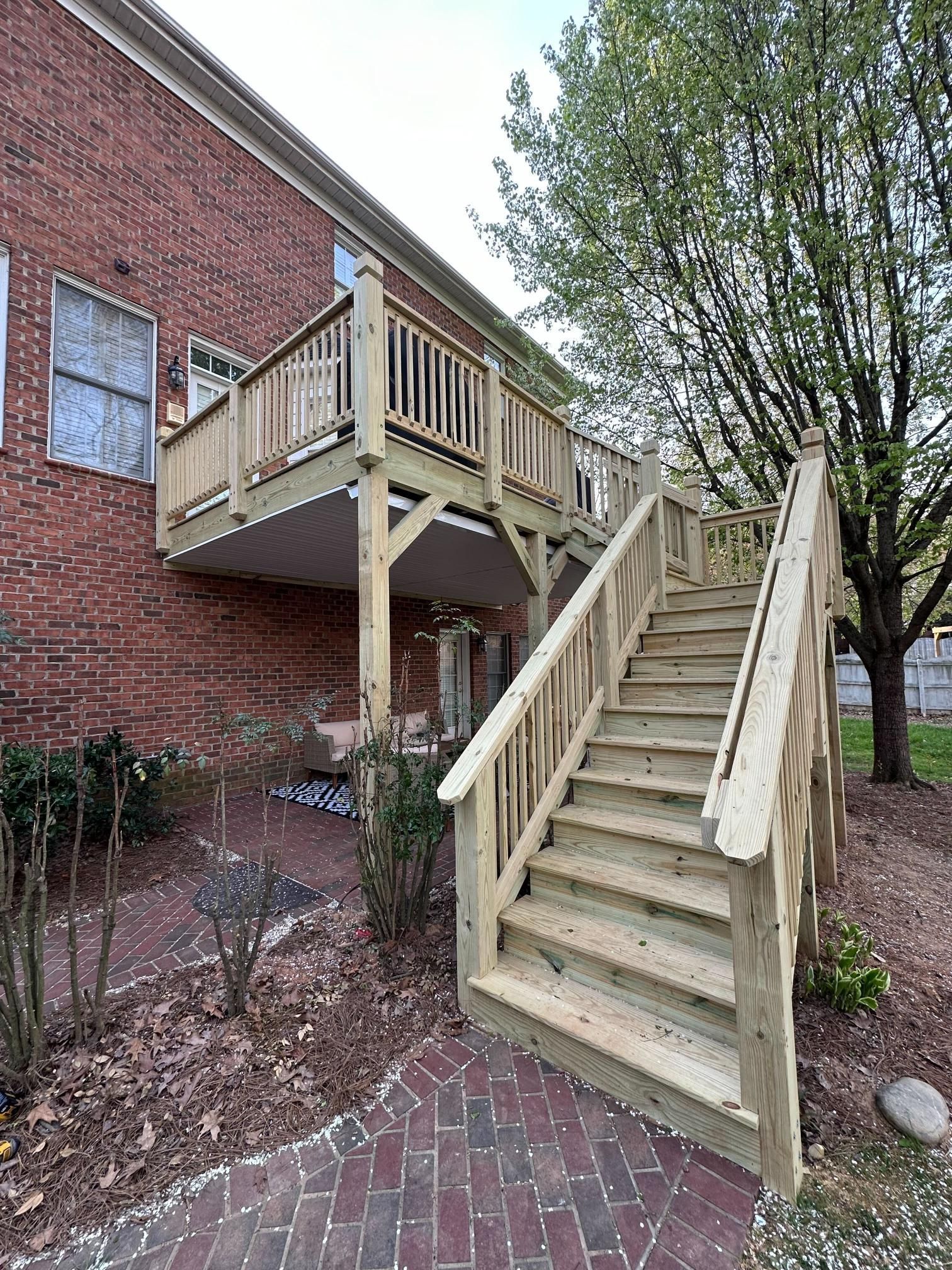 Wooden deck and stairs attached to a brick building in a yard with landscaping.