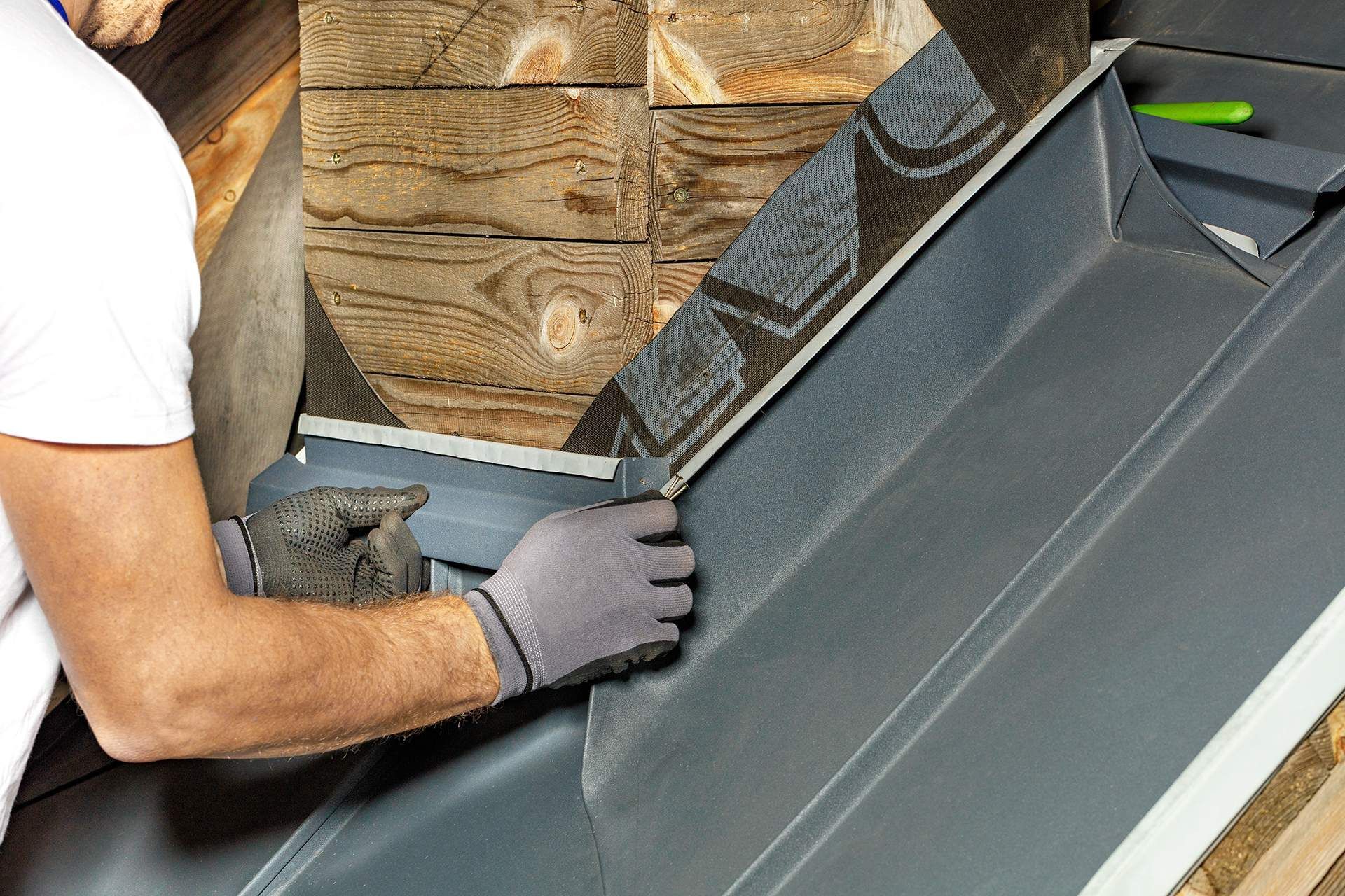 Person installing roofing with a staple gun, stapling flashing to a roof.