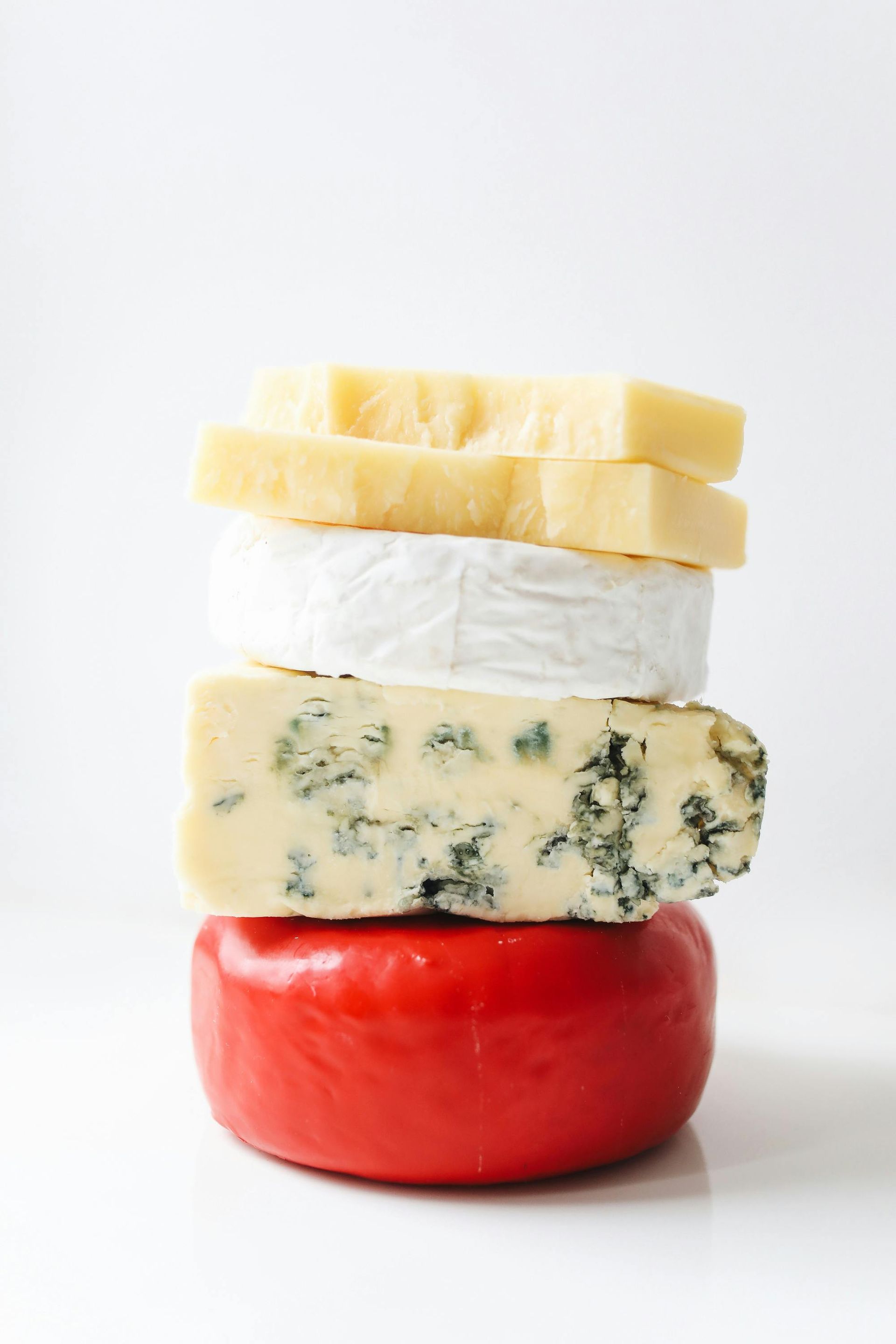 Stack of four cheeses: cheddar, brie, blue cheese, and red-waxed Gouda.