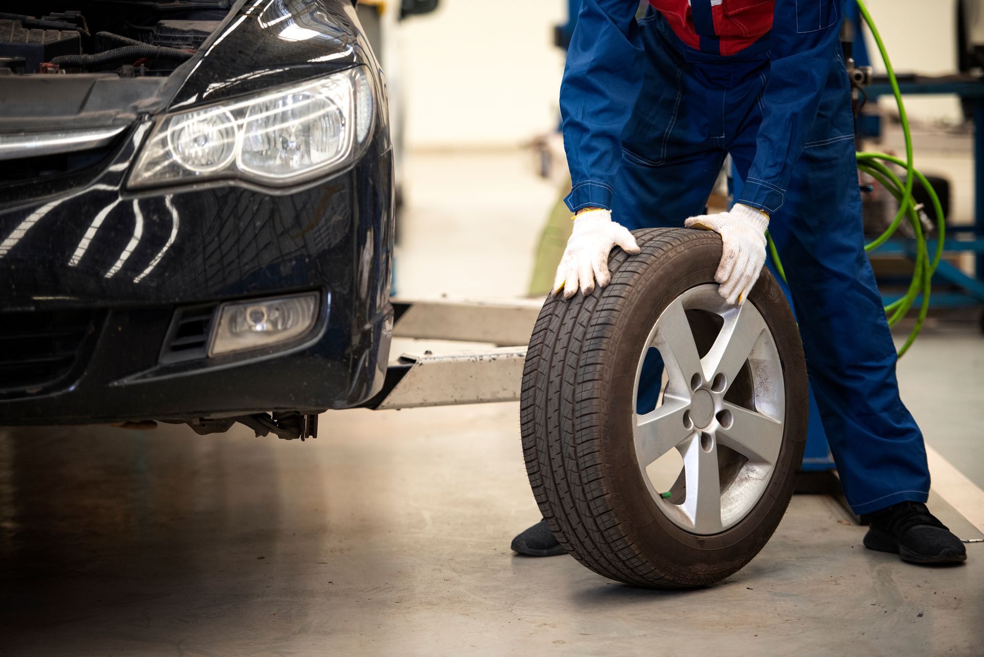 Mechanic rolling a tire beside a black car in an auto repair shop
