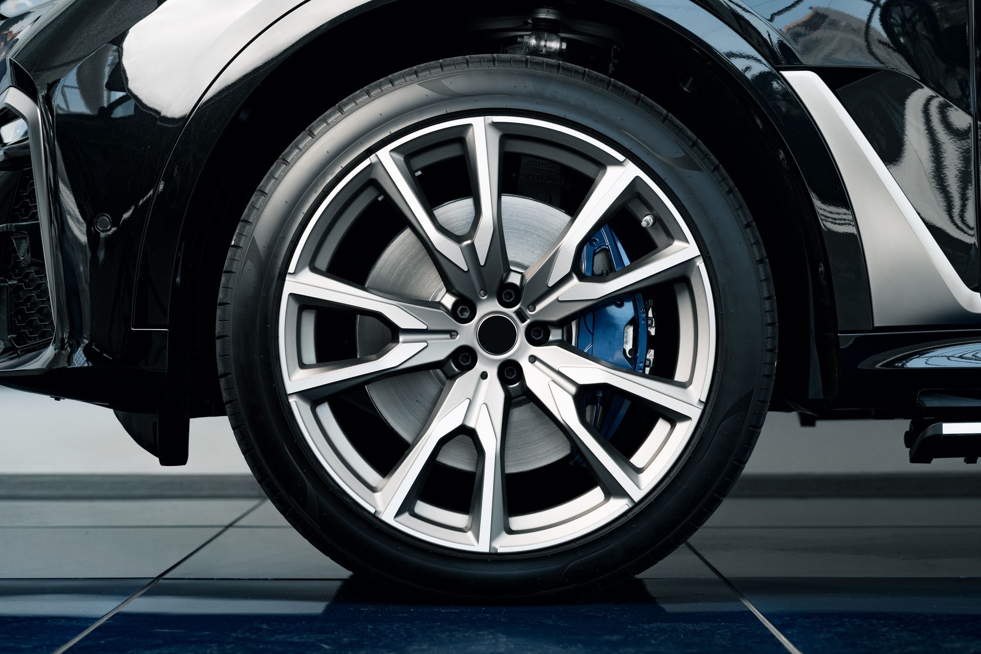Close-up of a black car’s silver alloy wheel and tire with a blue brake caliper