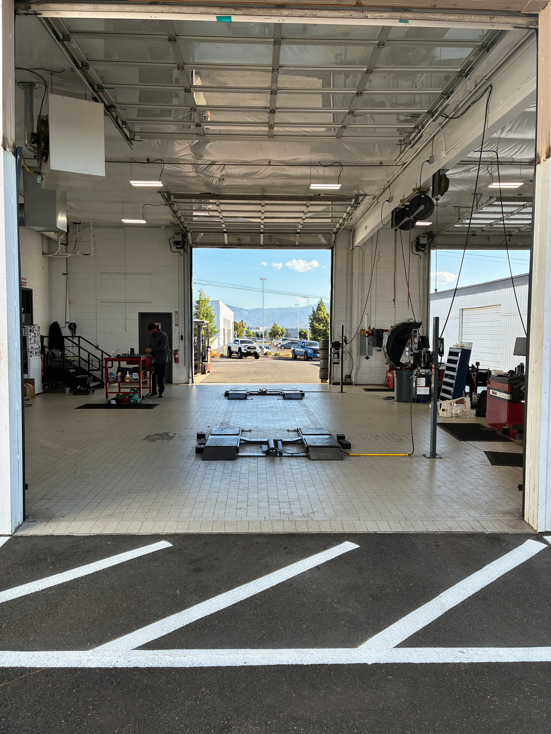 Empty auto repair bay with tools, open garage door, and sunlight visible outside.