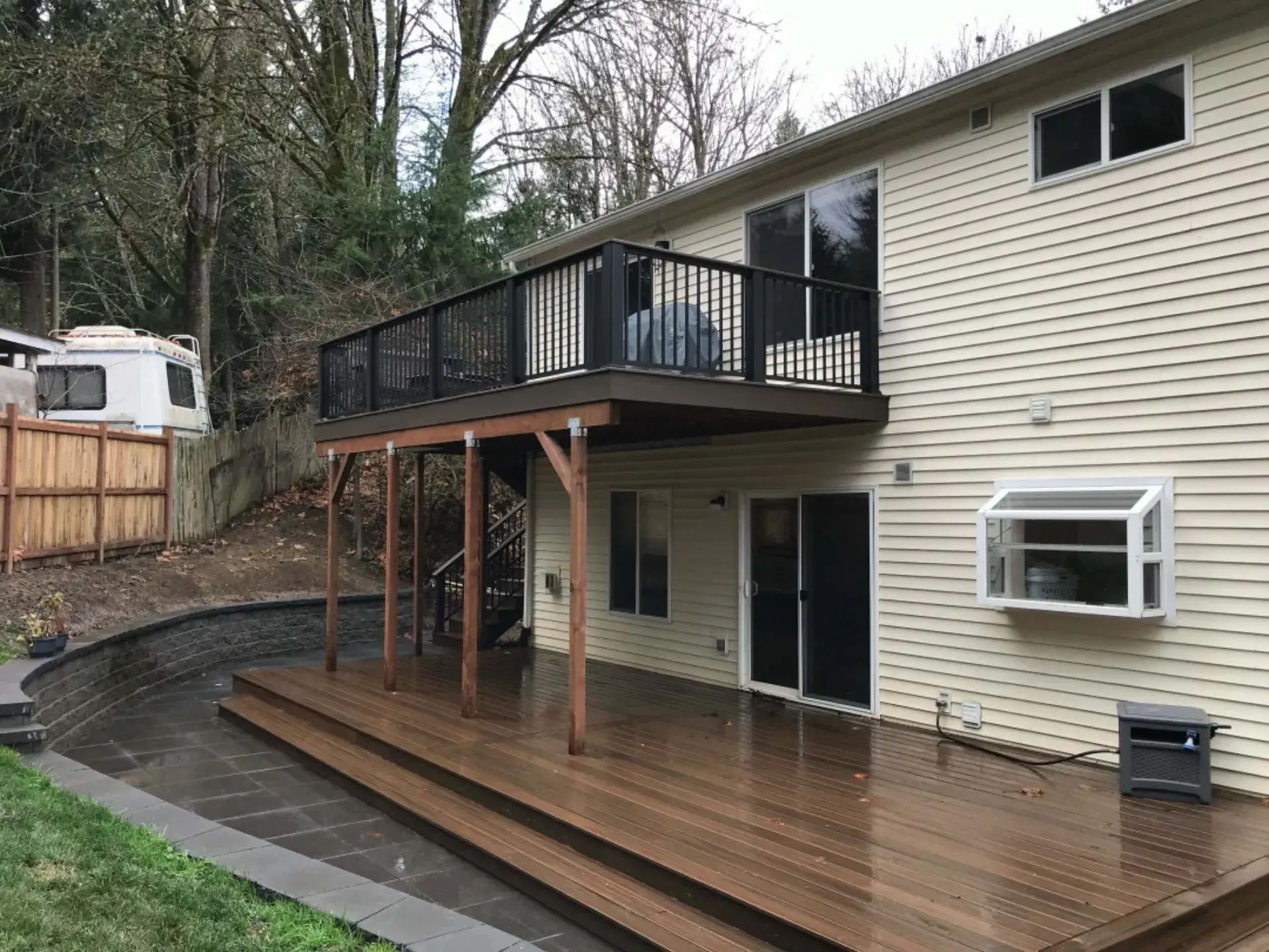 Wooden deck and covered patio beside beige house on a wooded hillside
