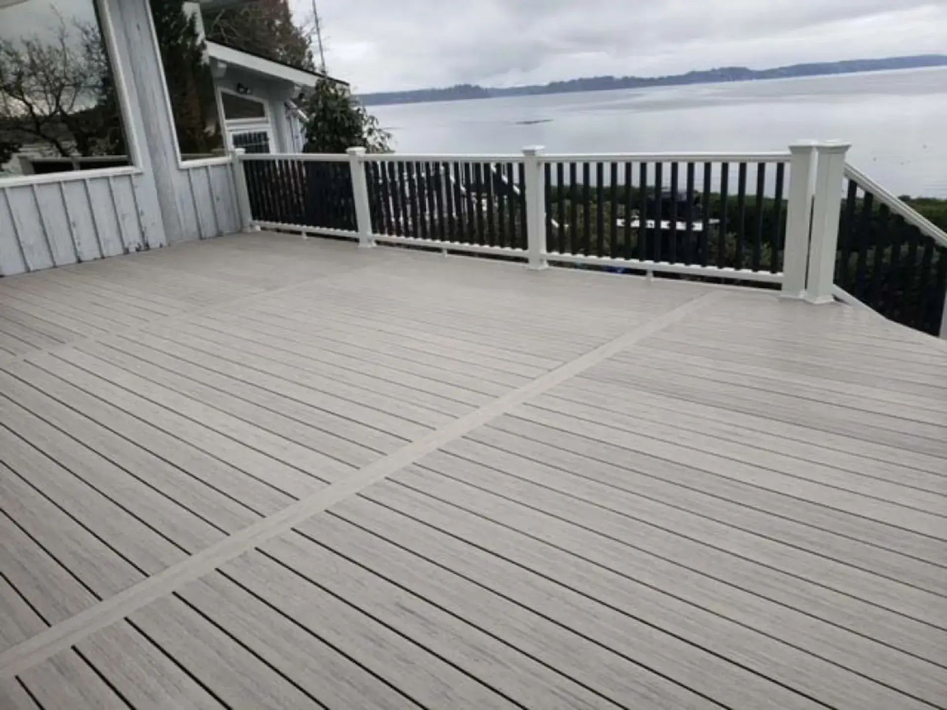 Spacious light-gray wooden deck with black railing overlooking water and trees