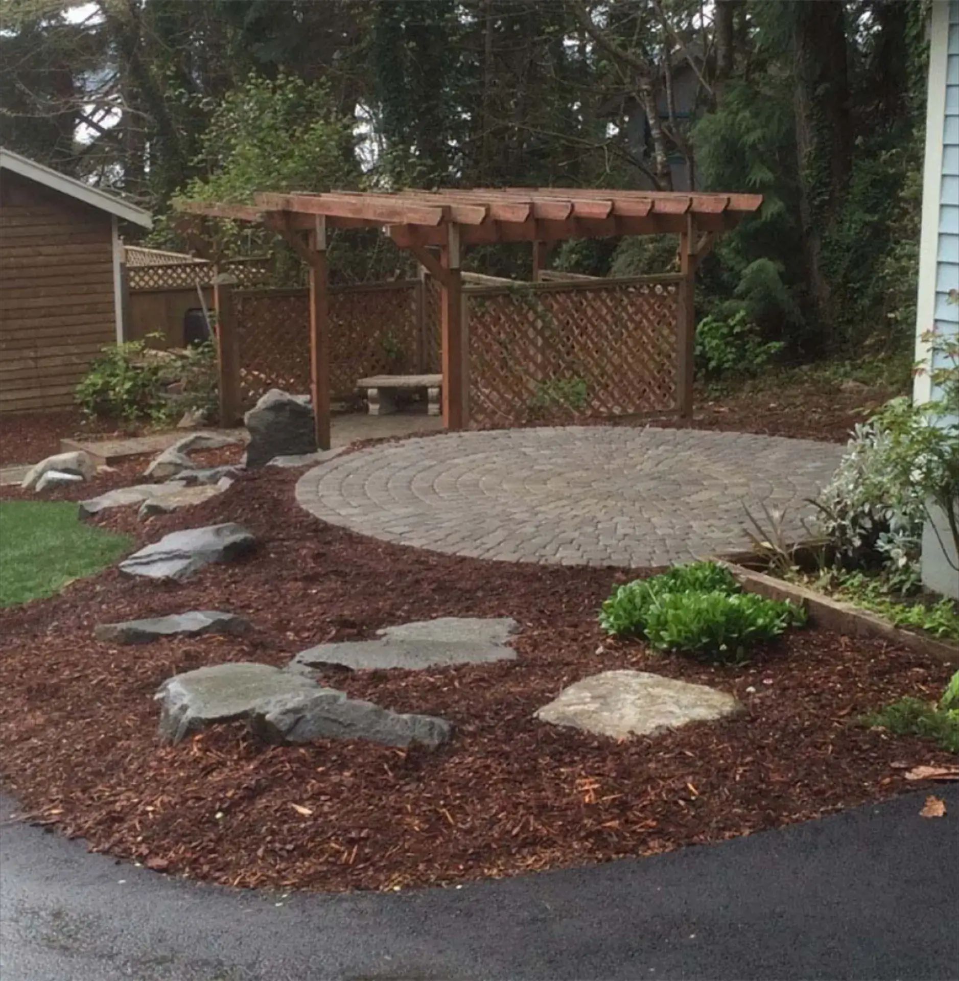 Backyard patio with wooden pergola, circular gravel area, stone steps, and landscaped mulch beds