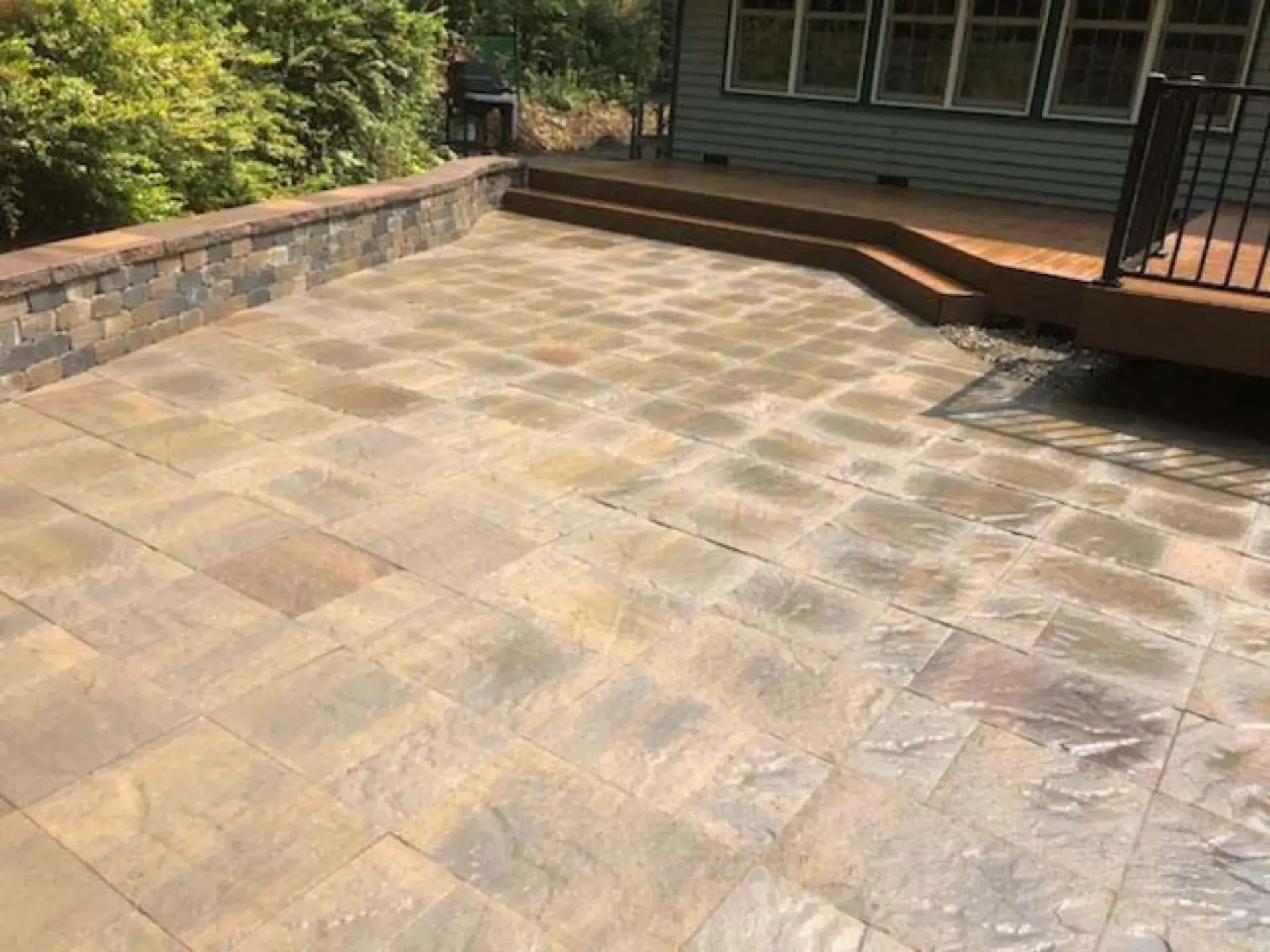 Stone patio with steps leading to a house deck and stone retaining wall along the side