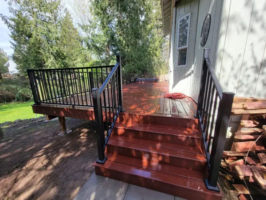 Red front porch steps with black railings leading to a house entrance, with a deck and yard beside it