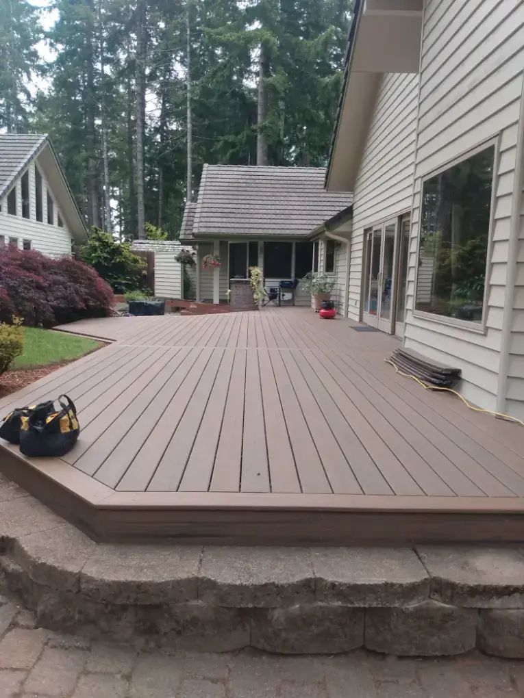 Backyard wooden deck with house siding, stone steps, and a small shed in the distance