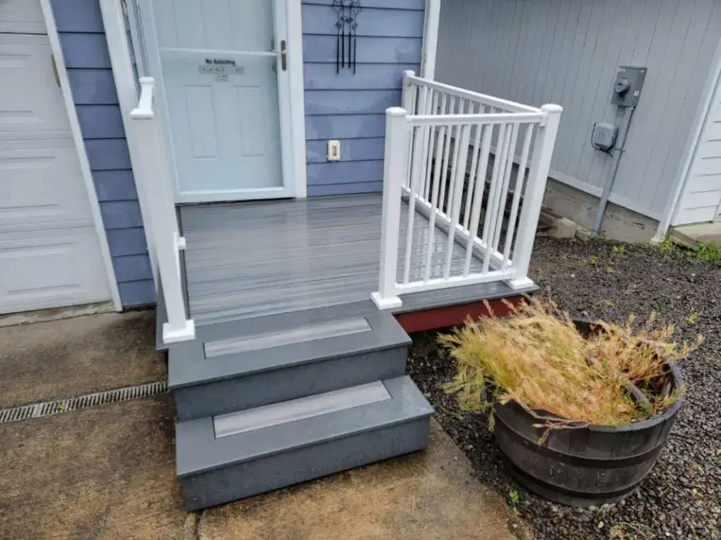 Front porch with gray steps, white railing, and a pale blue door beside a planter with dried plants