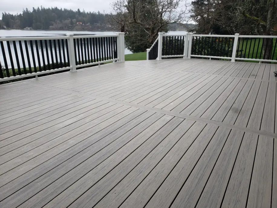 Empty gray wooden deck with white railing overlooking a lake and trees