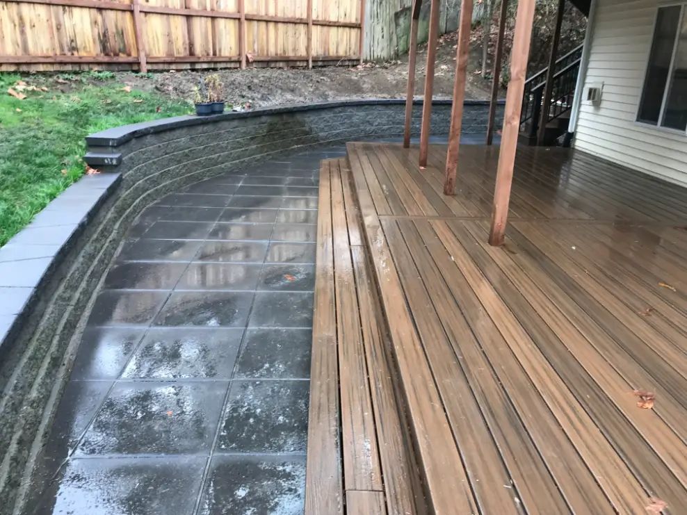 Curved concrete pool edge beside a wet wooden deck and covered patio in a backyard
