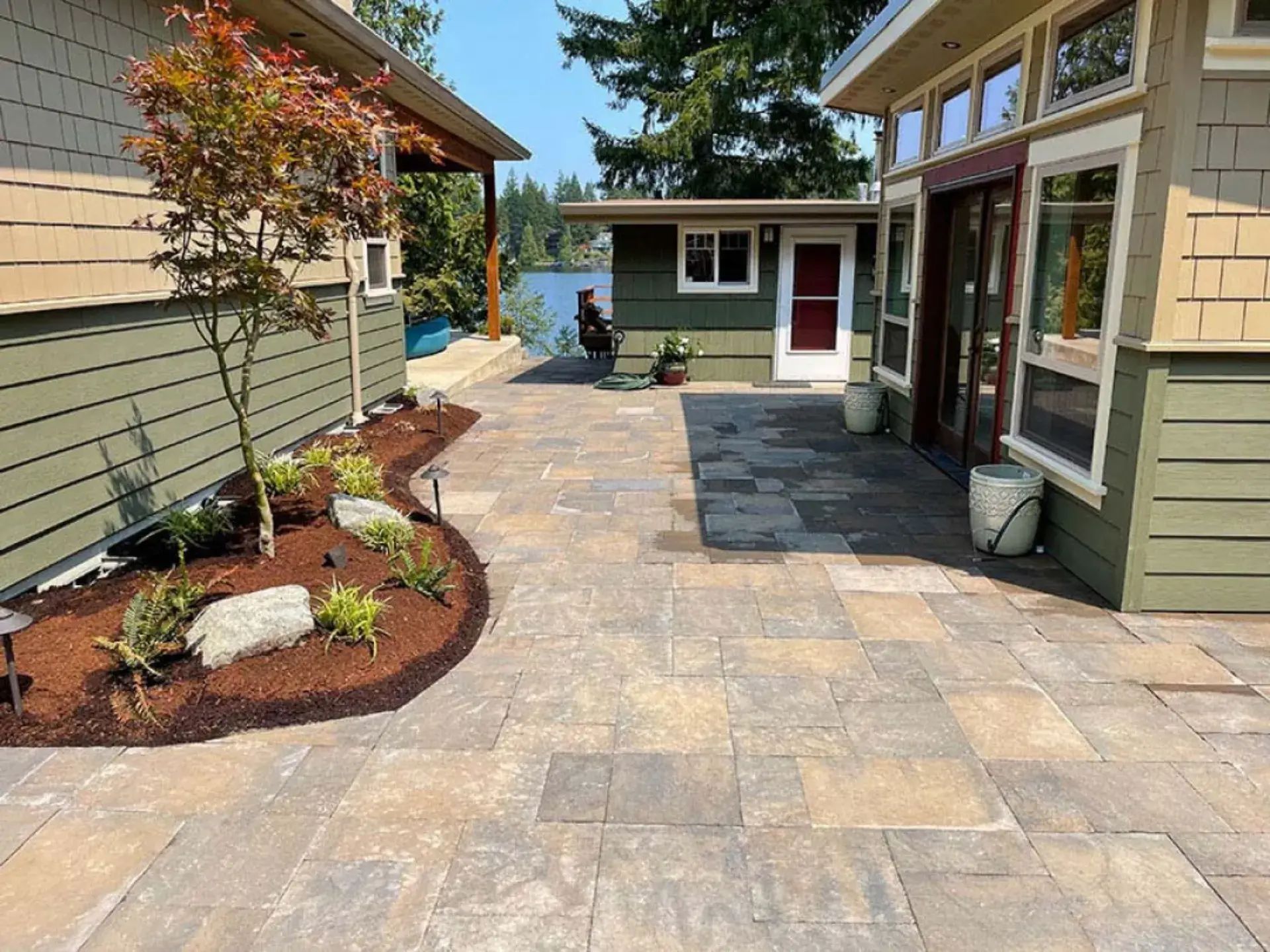 Stone patio walkway between two houses with potted plants and a view of the water ahead