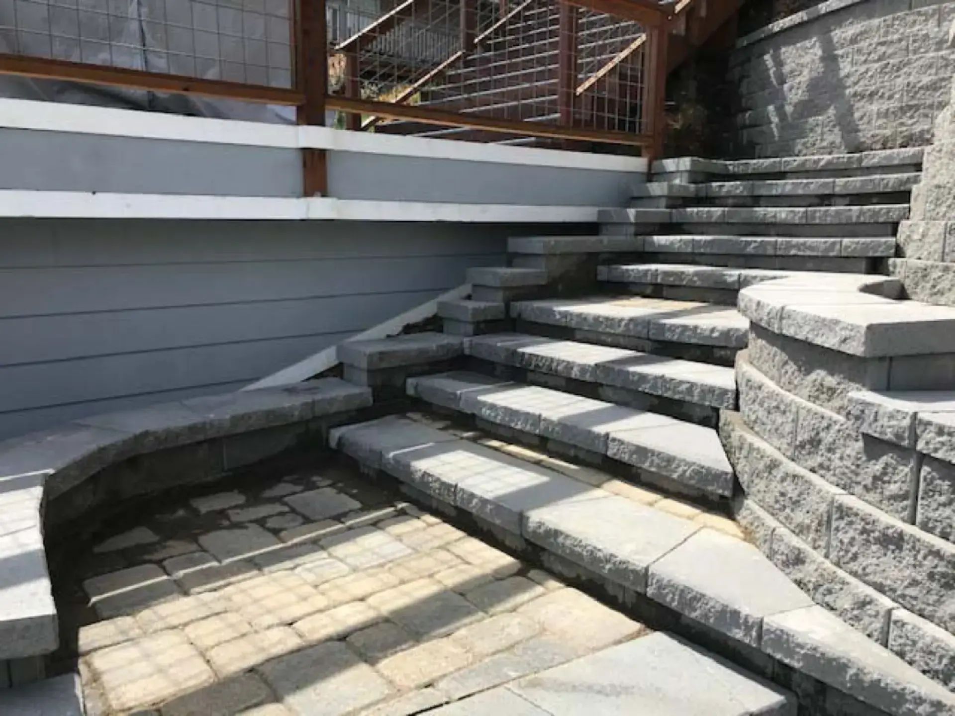 Stone steps and a curved retaining wall leading to a raised patio with a wooden fence above.