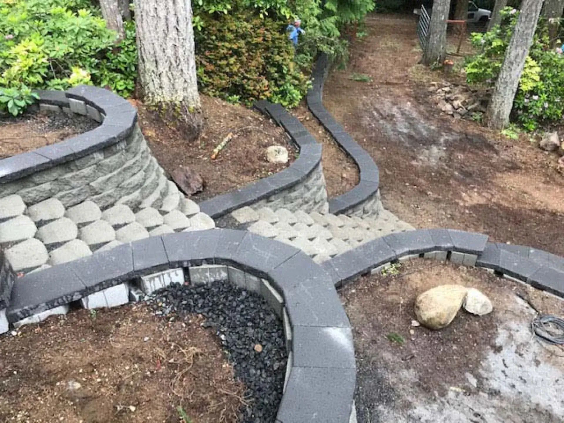 Curved stone garden edging around a tree and soil bed beside a dirt path and pavers