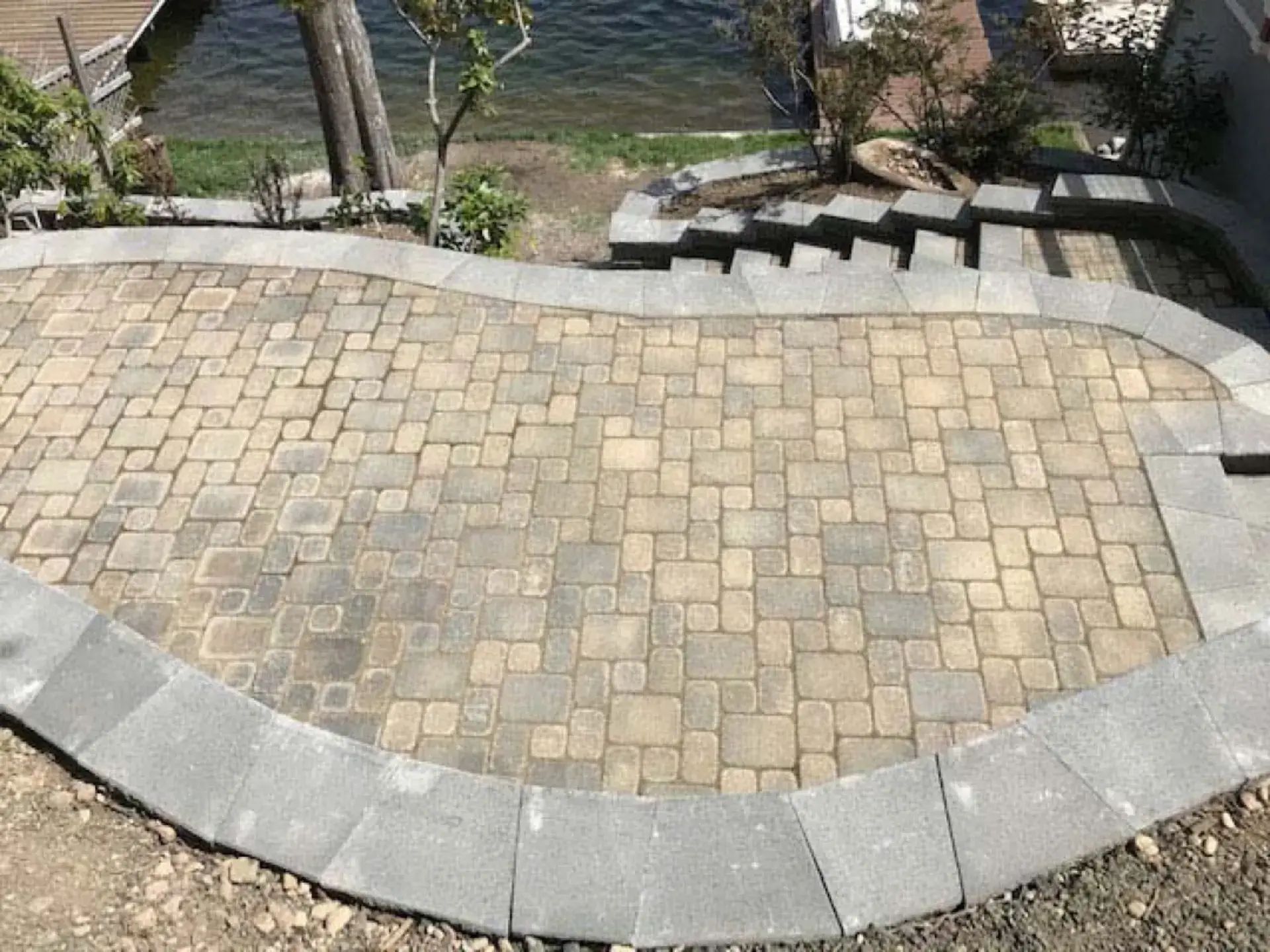 Curved stone patio with tan pavers and gray border beside a garden walkway