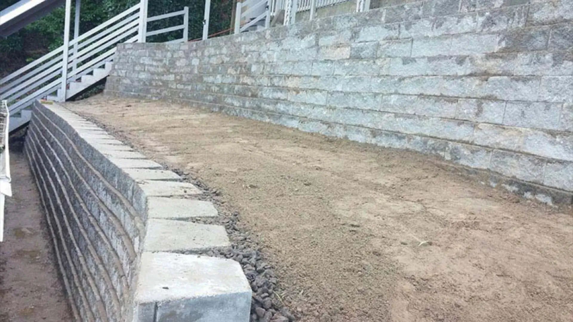 Stepped dirt ramp beside a stone retaining wall and concrete walkway outdoors