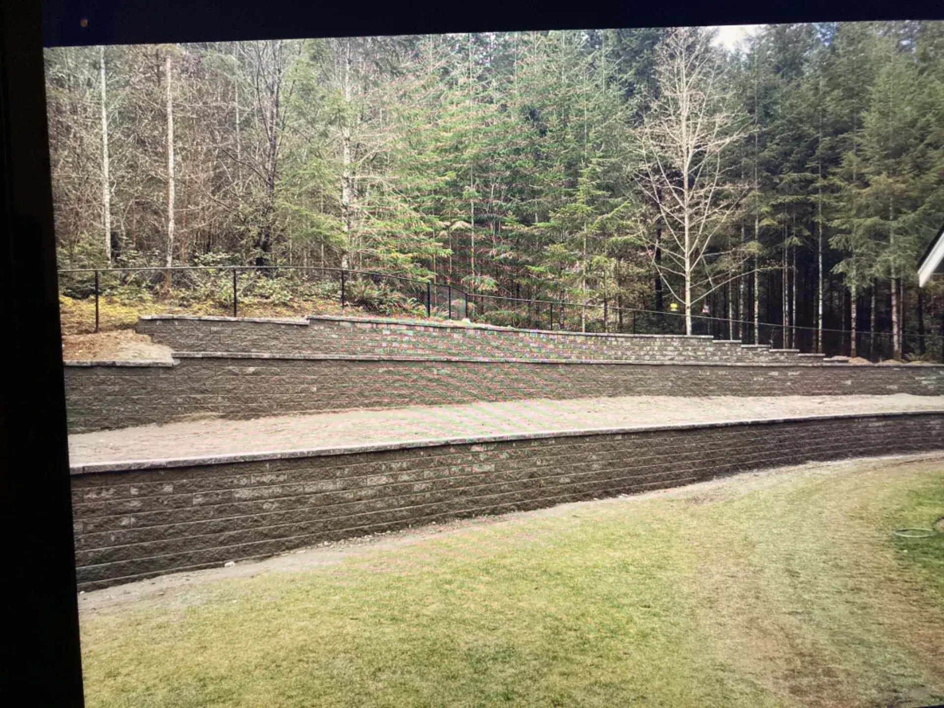 Terraced stone steps and a grassy lawn beside a wooded hillside under trees.
