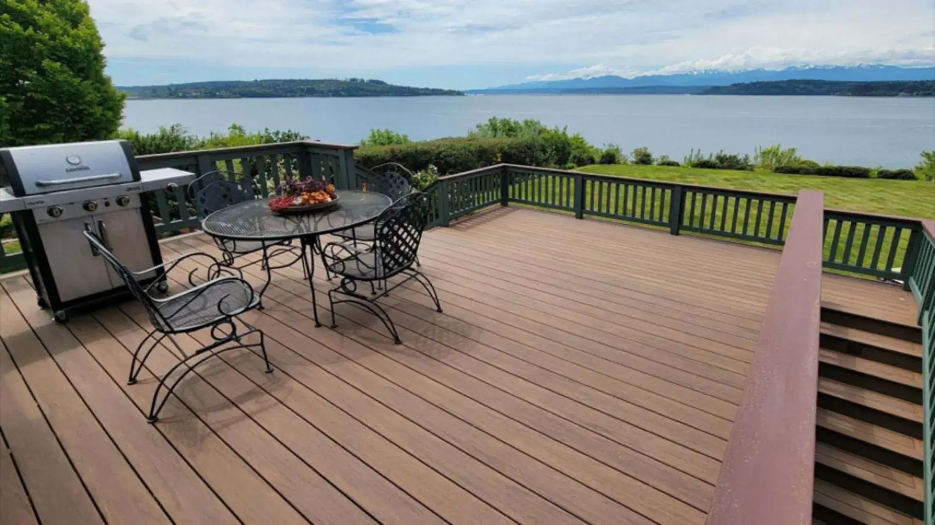 Wooden deck with patio table and grill overlooking a lake and distant mountains