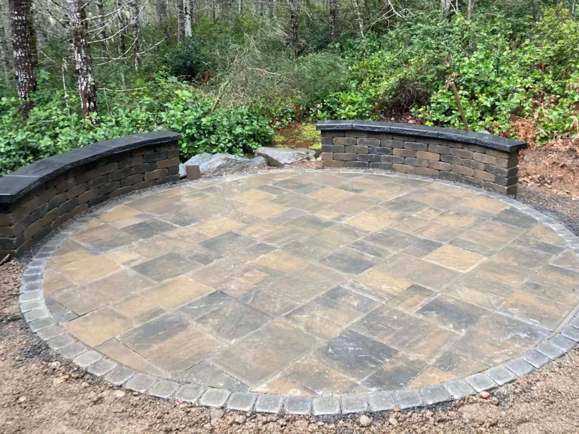 Circular stone patio with curved brick benches in a wooded garden setting
