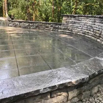 Wet stone patio with curved retaining walls in a wooded outdoor setting