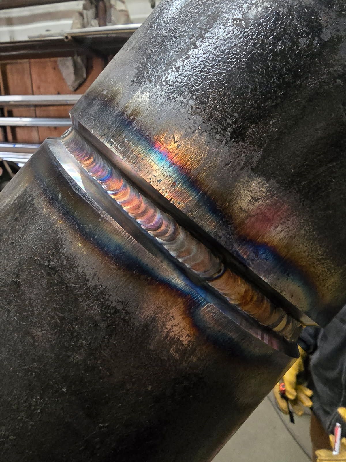 Welded pipe joint; rainbow-colored heat discoloration on metal, showing weld beads.